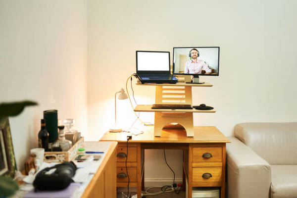 Young man talking on a video monitor sitting on a standing desk in a makeshift home office